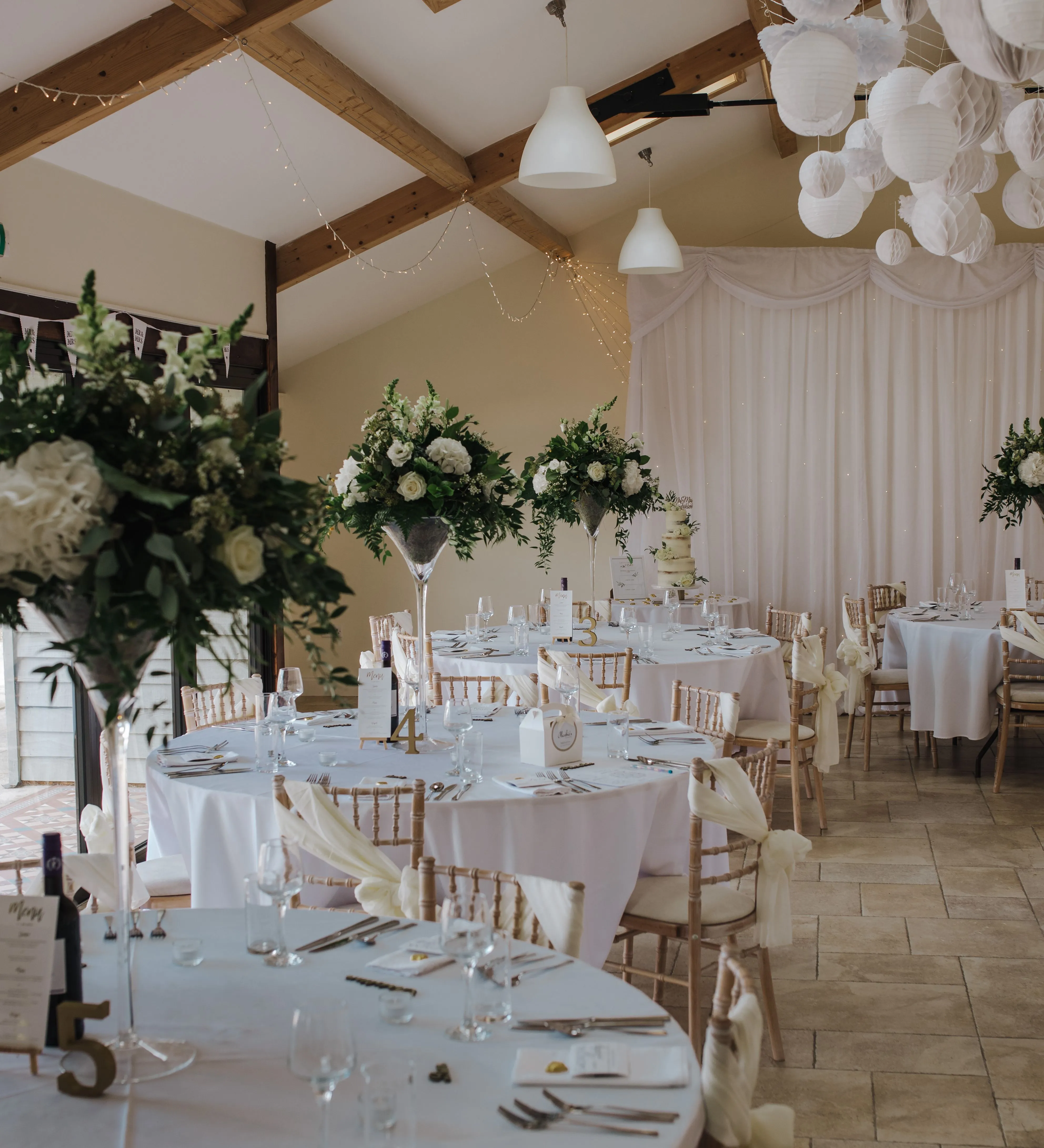 Elegant wedding reception room with round tables, white tablecloths, floral centrepieces and hanging paper lanterns