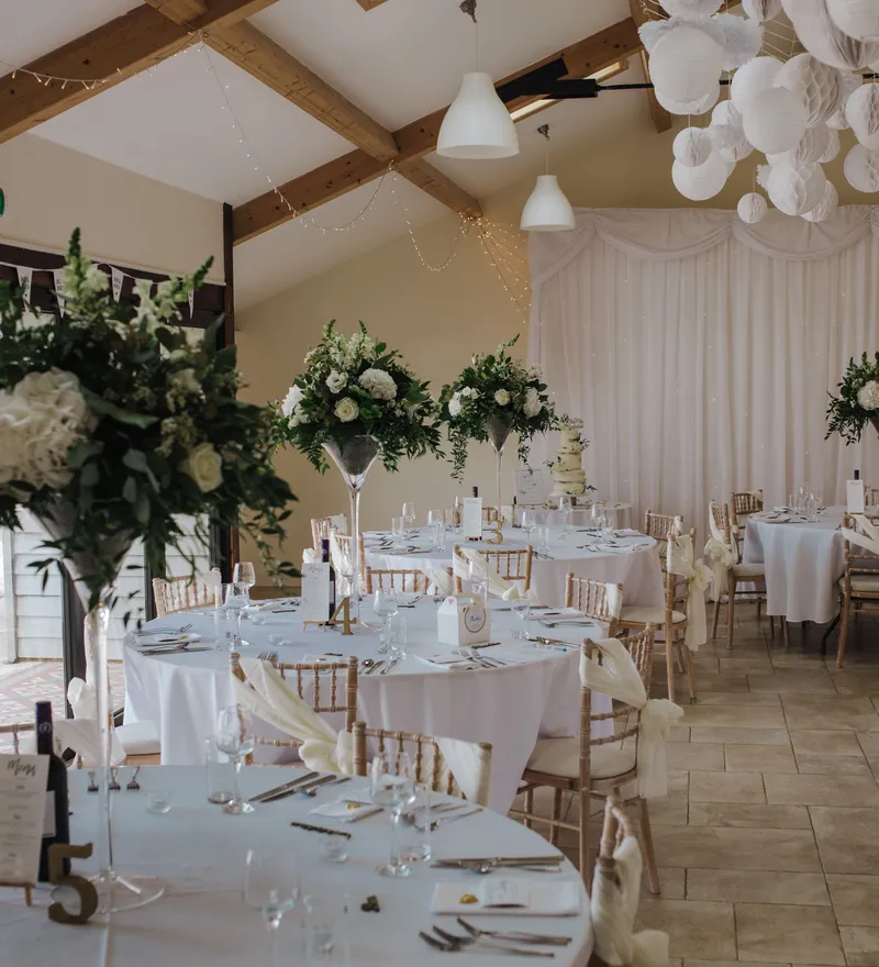 Elegant wedding reception room with round tables, white tablecloths, floral centrepieces and hanging paper lanterns