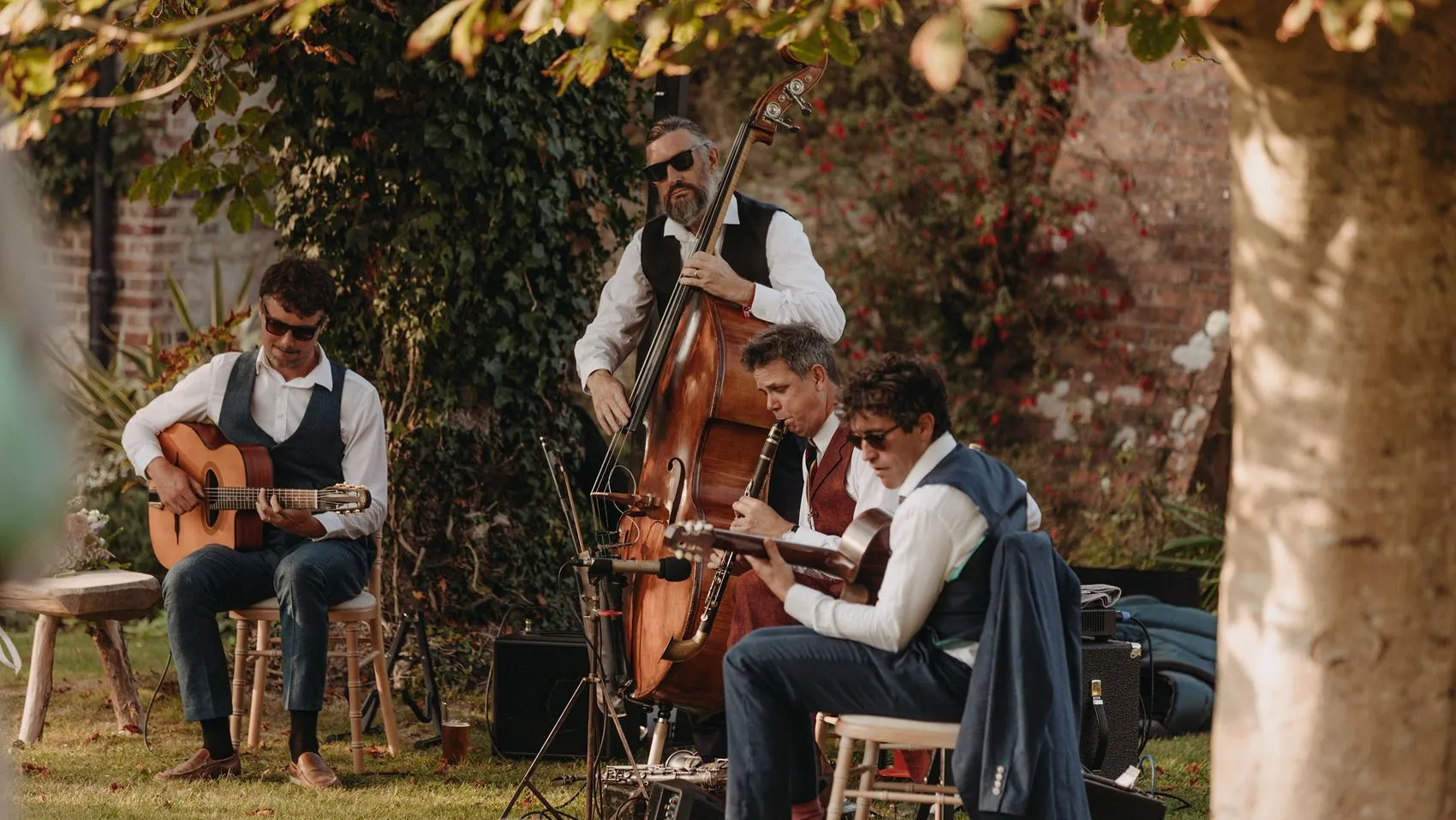 Musicians playing guitar, double bass and clarinet in a garden setting