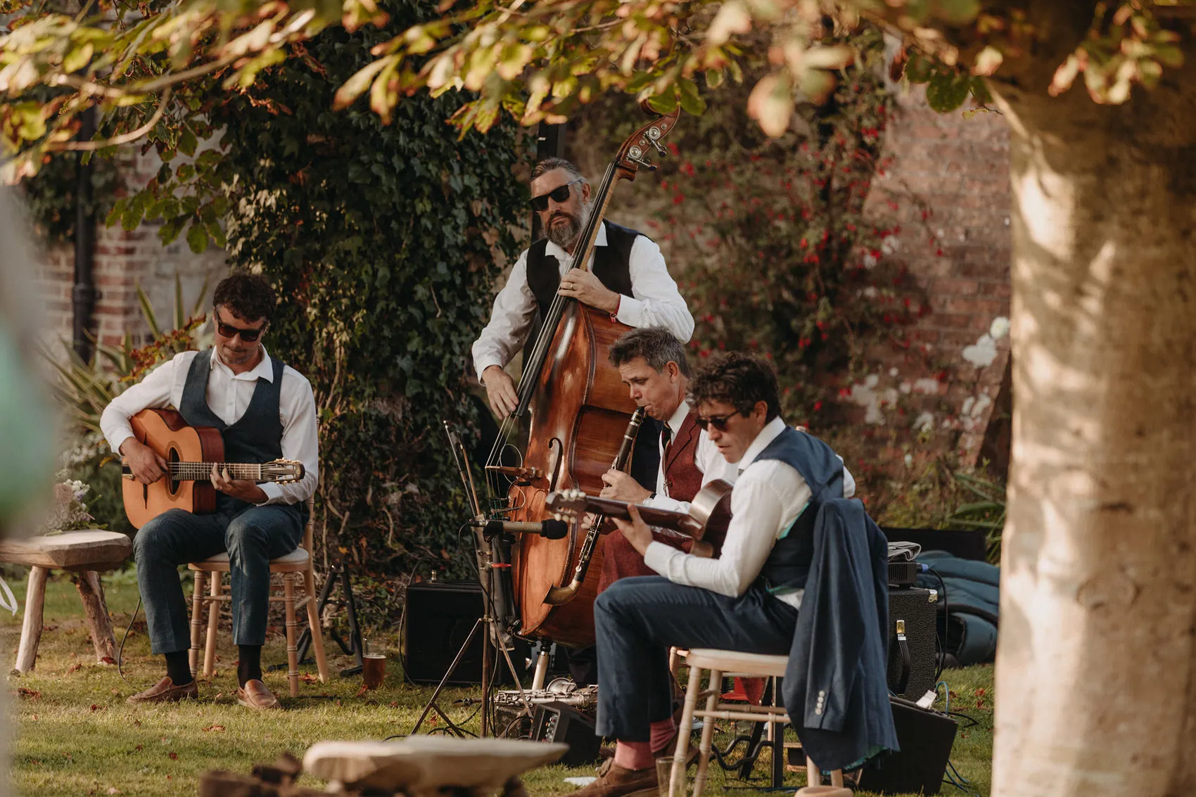 Musicians playing guitar, double bass and clarinet in a garden setting