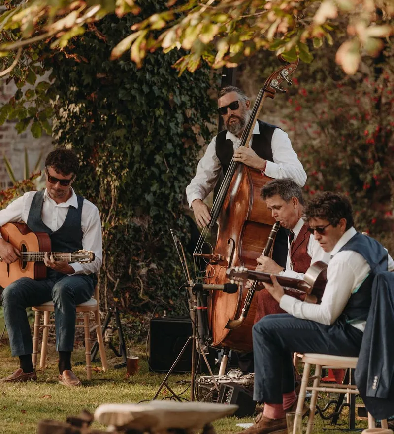 Musicians playing guitar, double bass and clarinet in a garden setting