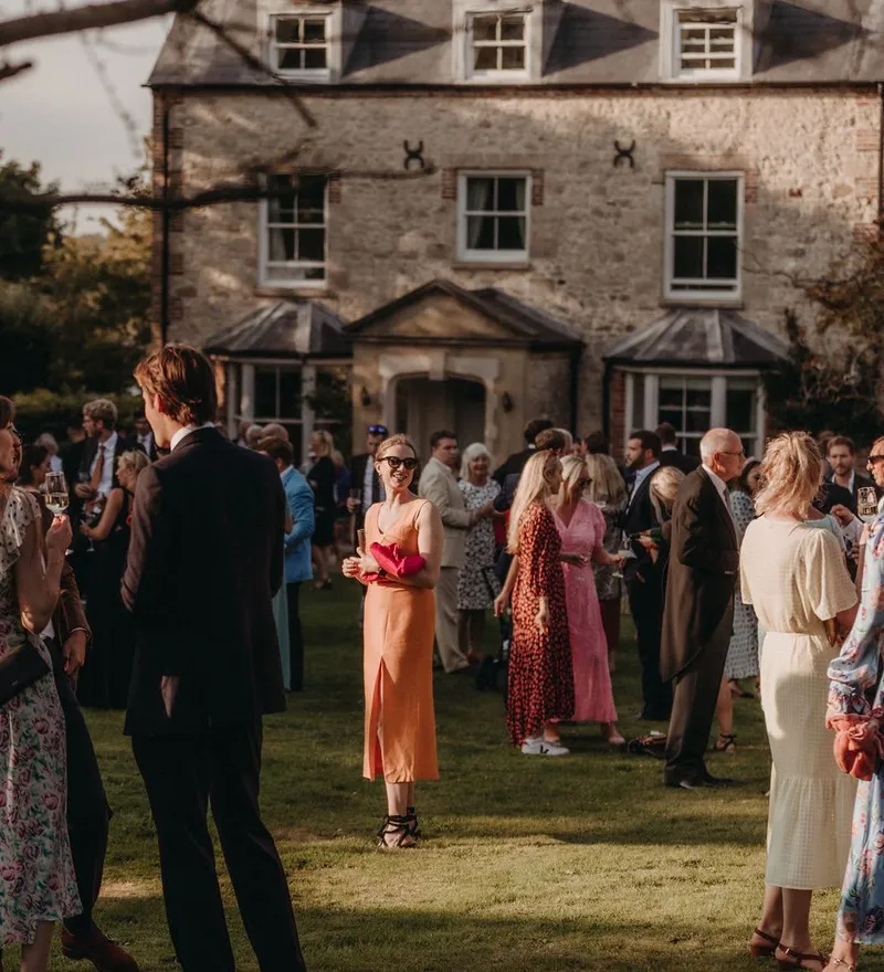 Guests socialising on a lawn outside a large stone country house