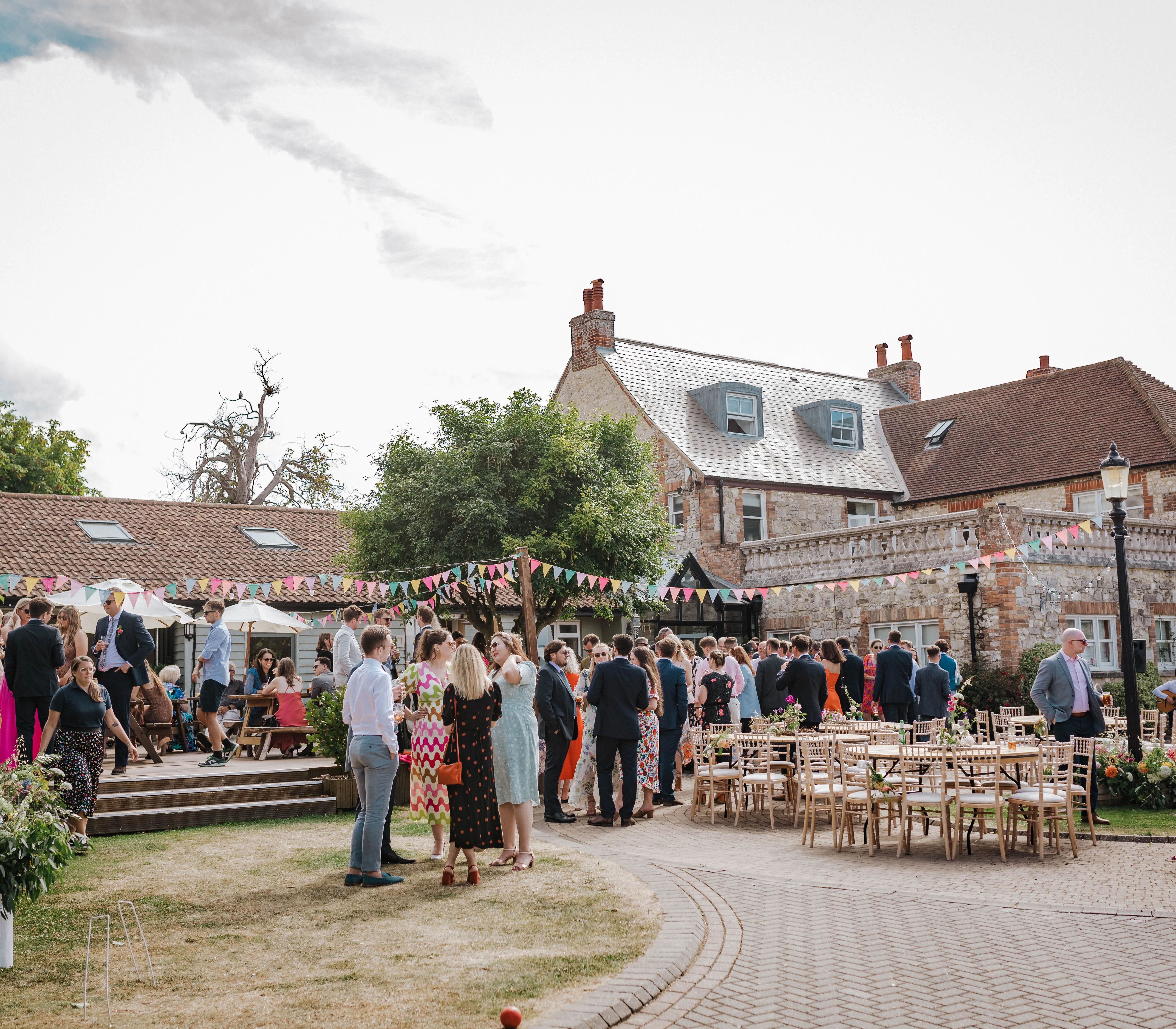 Guests socialising in a courtyard outside a stone country house decorated with bunting and outdoor tables