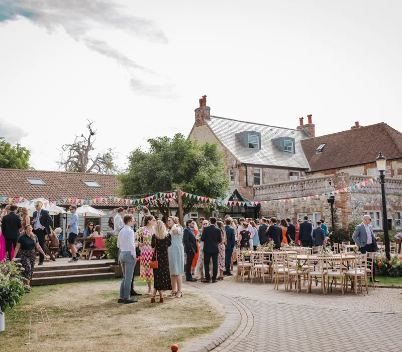 Guests socialising in a courtyard outside a stone country house decorated with bunting and outdoor tables
