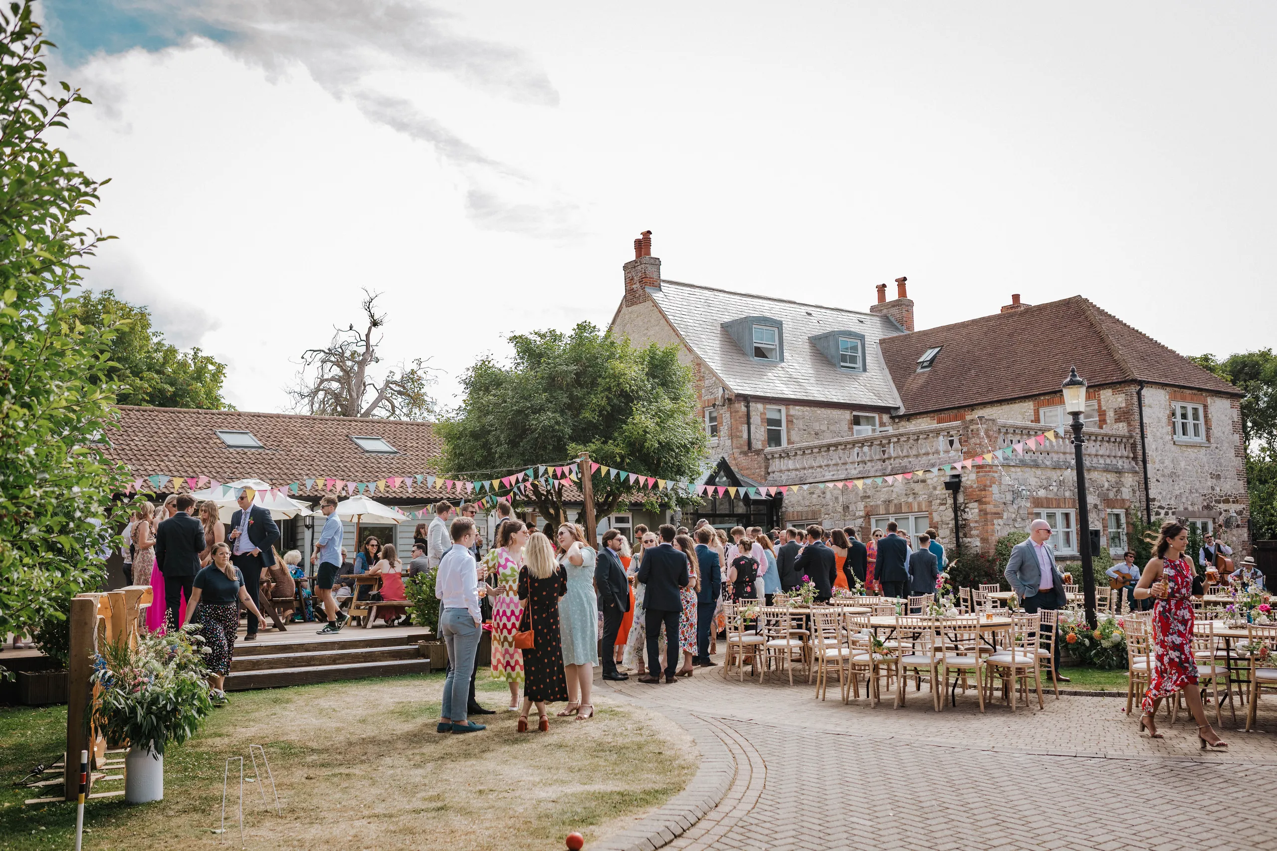 Guests socialising in a courtyard outside a stone country house decorated with bunting and outdoor tables