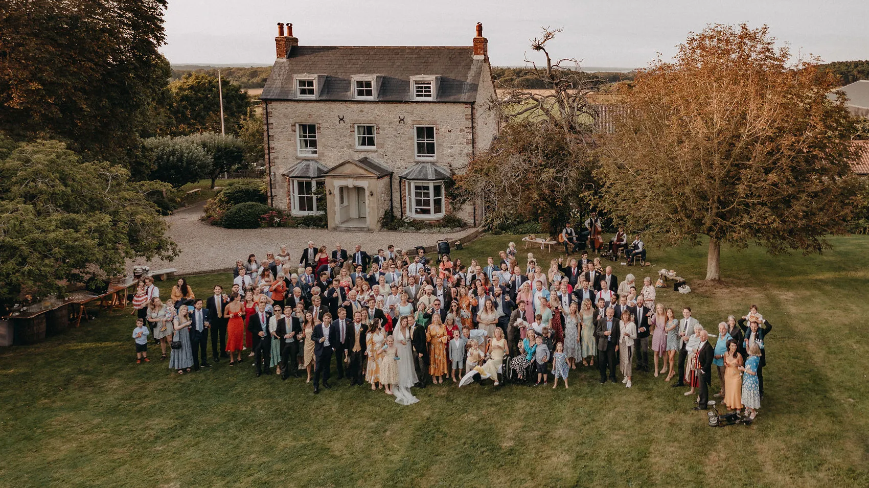 Large wedding group photo on a lawn in front of a country house