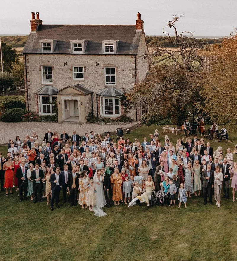 Large wedding group photo on a lawn in front of a country house