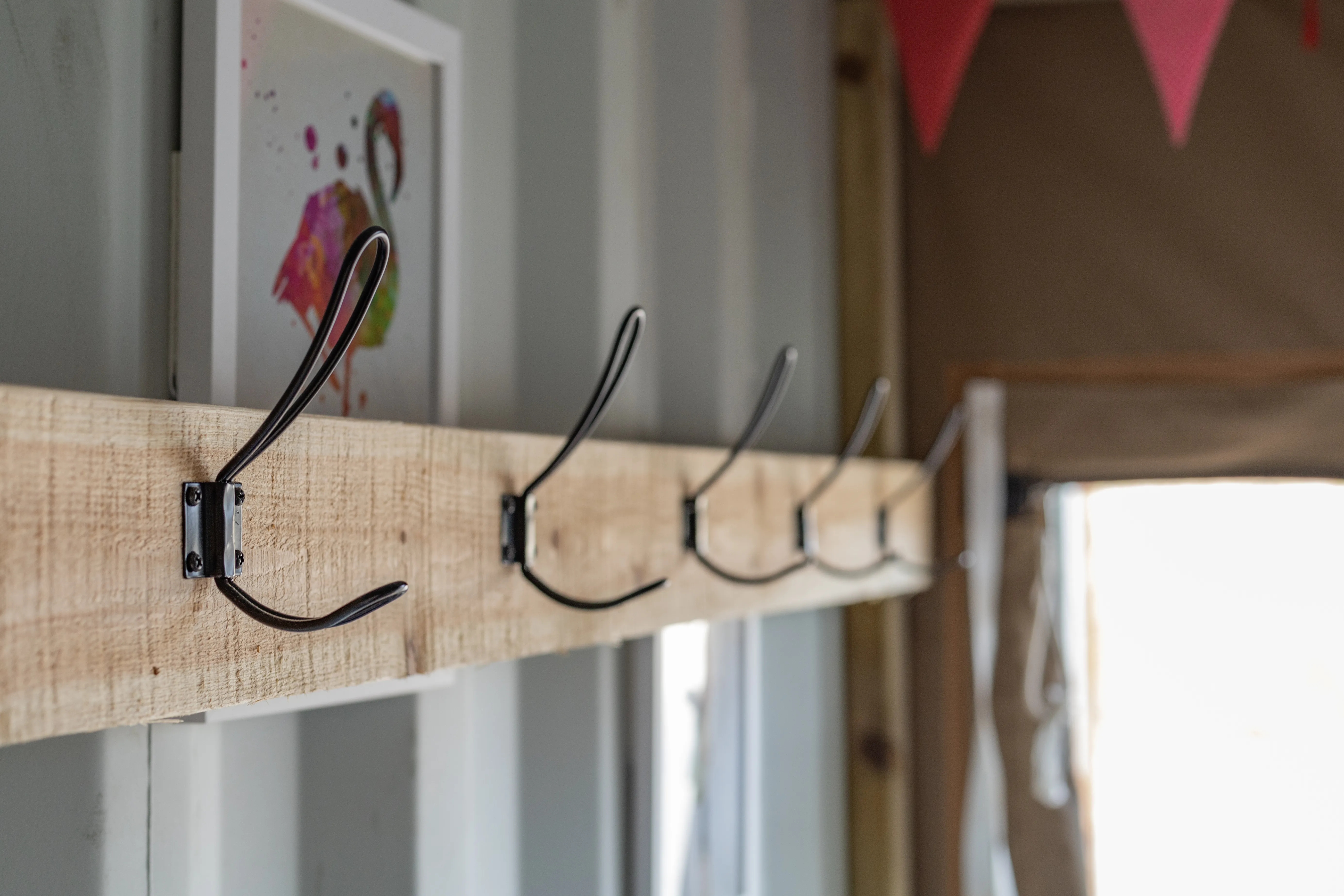Wooden coat rack with black metal hooks inside a cabin