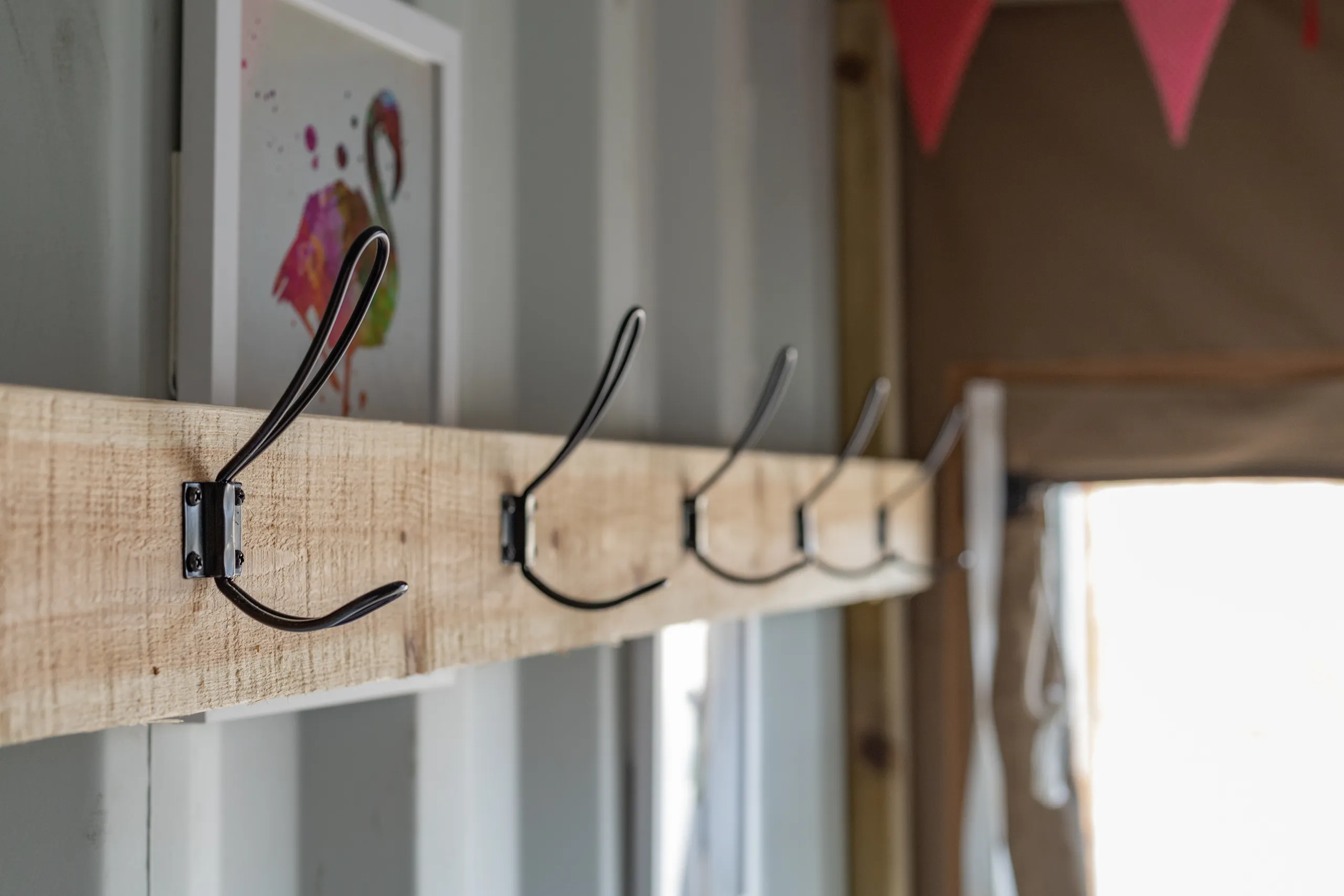 Wooden coat rack with black metal hooks inside a cabin