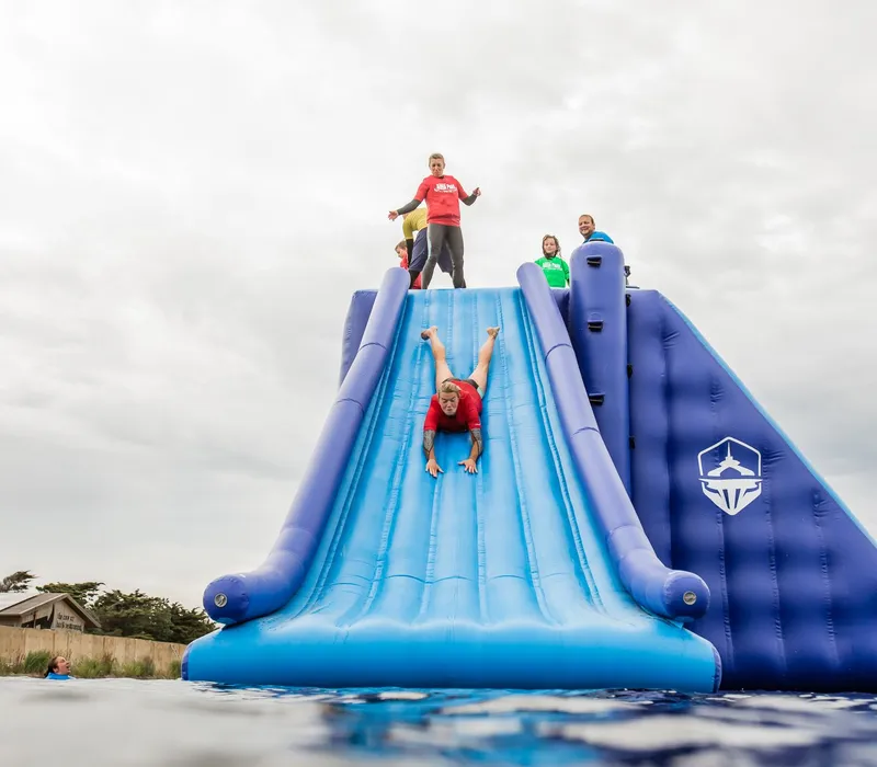 People on a large inflatable water slide, with one person sliding down headfirst into the water.