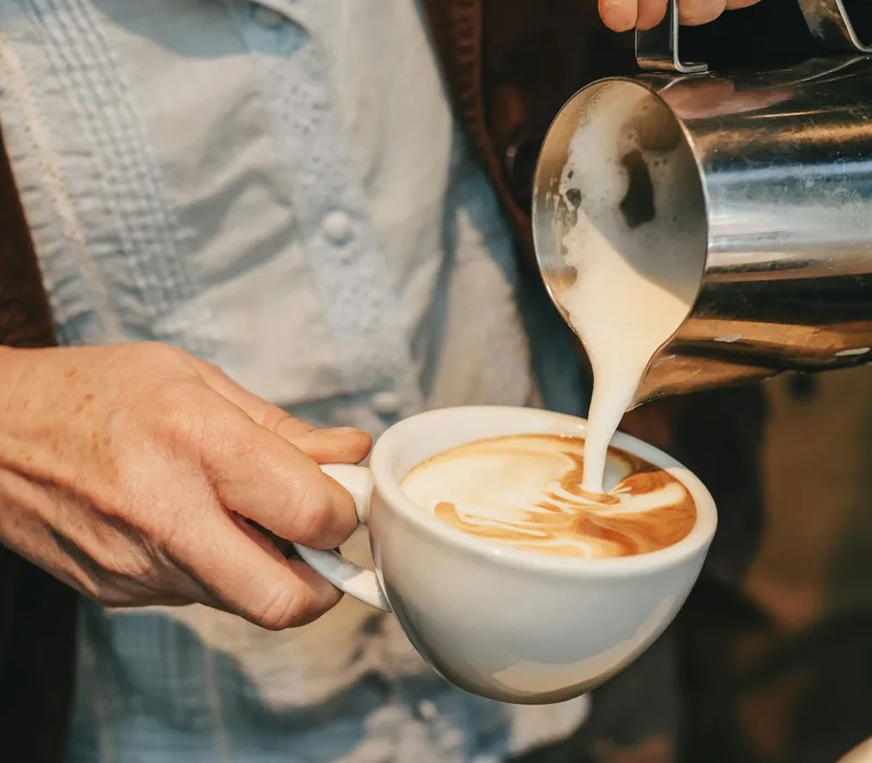 Barista pouring steamed milk into a cup of coffee to create latte art