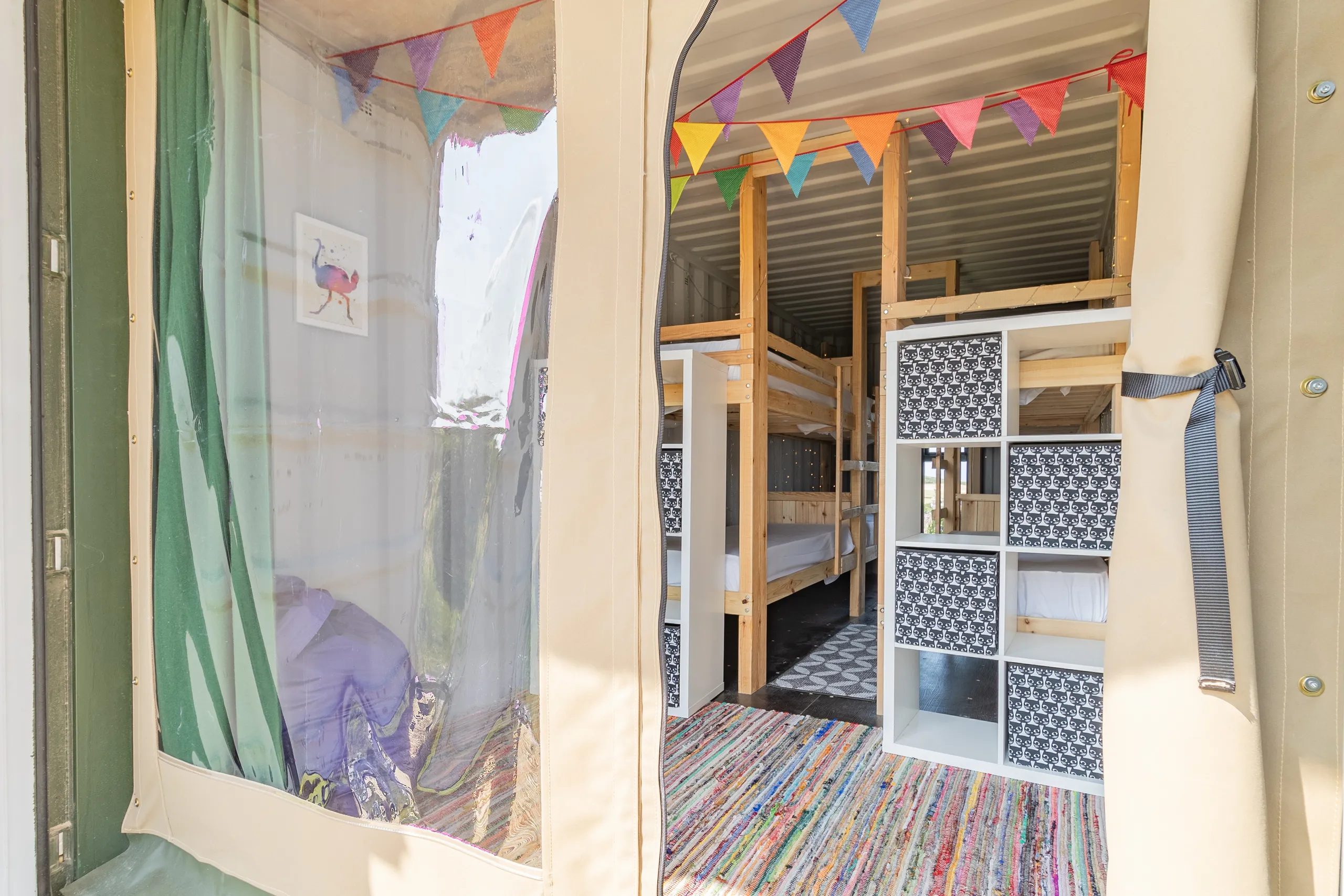Entrance to a family glamping container with bunk beds, colourful bunting and storage shelves