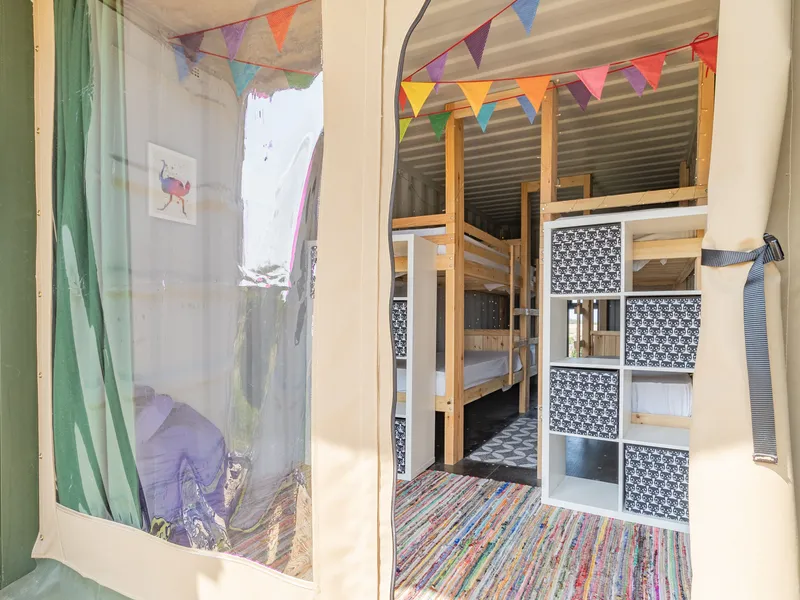 Entrance to a family glamping container with bunk beds, colourful bunting and storage shelves