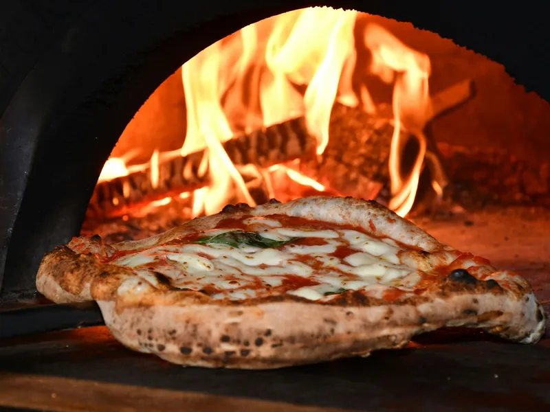 Wood-fired pizza baking in a brick oven with flames in the background