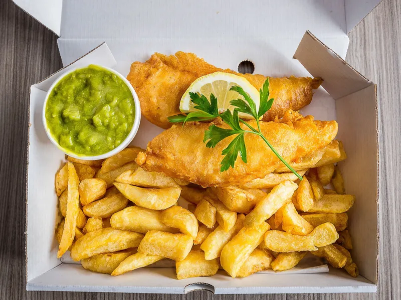 Fish and chips in a takeaway box with mushy peas, lemon and parsley