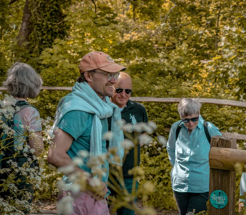 Group of hikers chatting by a wooden gate on a leafy woodland trail