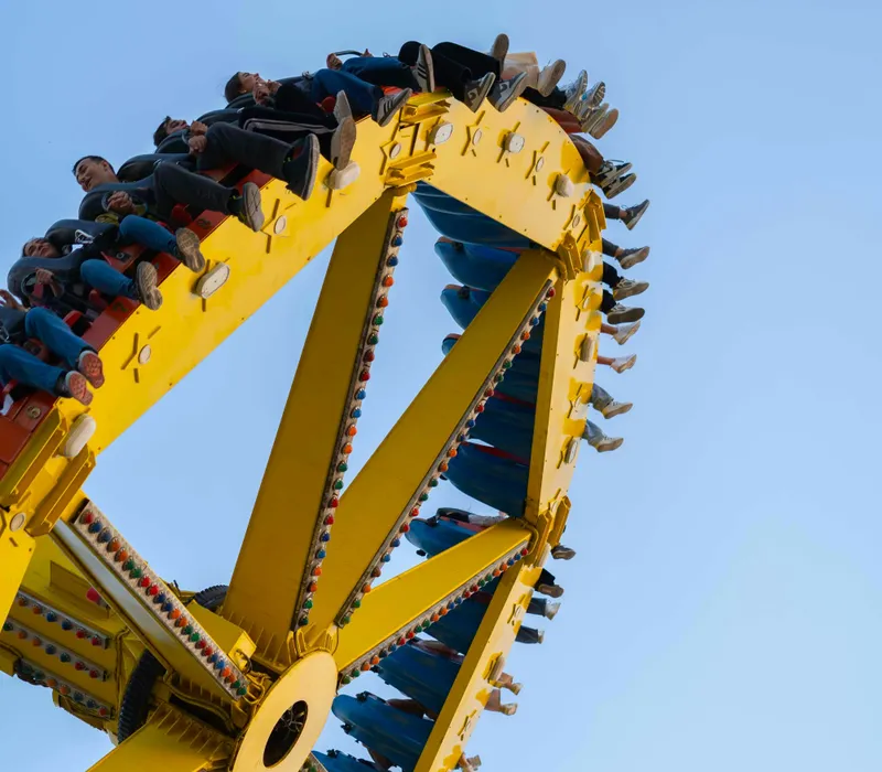 People riding a yellow spinning fairground ride against a clear blue sky