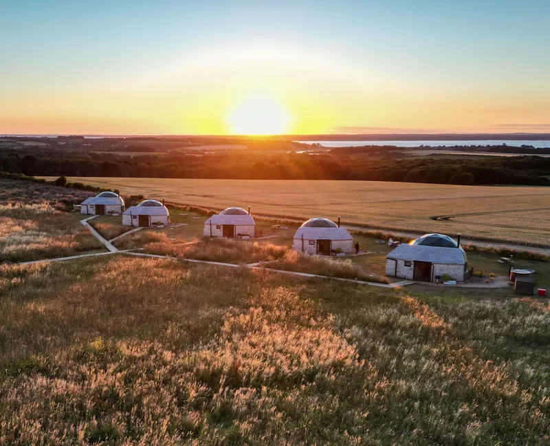 Sunset over countryside with a row of small dome cabins in a grassy field