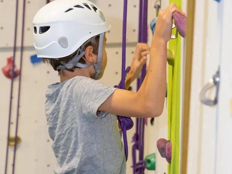 Child wearing a helmet and climbing harness climbing an indoor rock wall