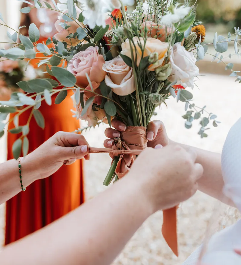 Hands tying a ribbon around a bridal bouquet of pale roses and eucalyptus greenery