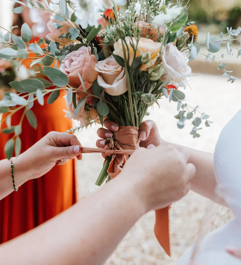 Hands tying a ribbon around a bridal bouquet of pale roses and eucalyptus greenery