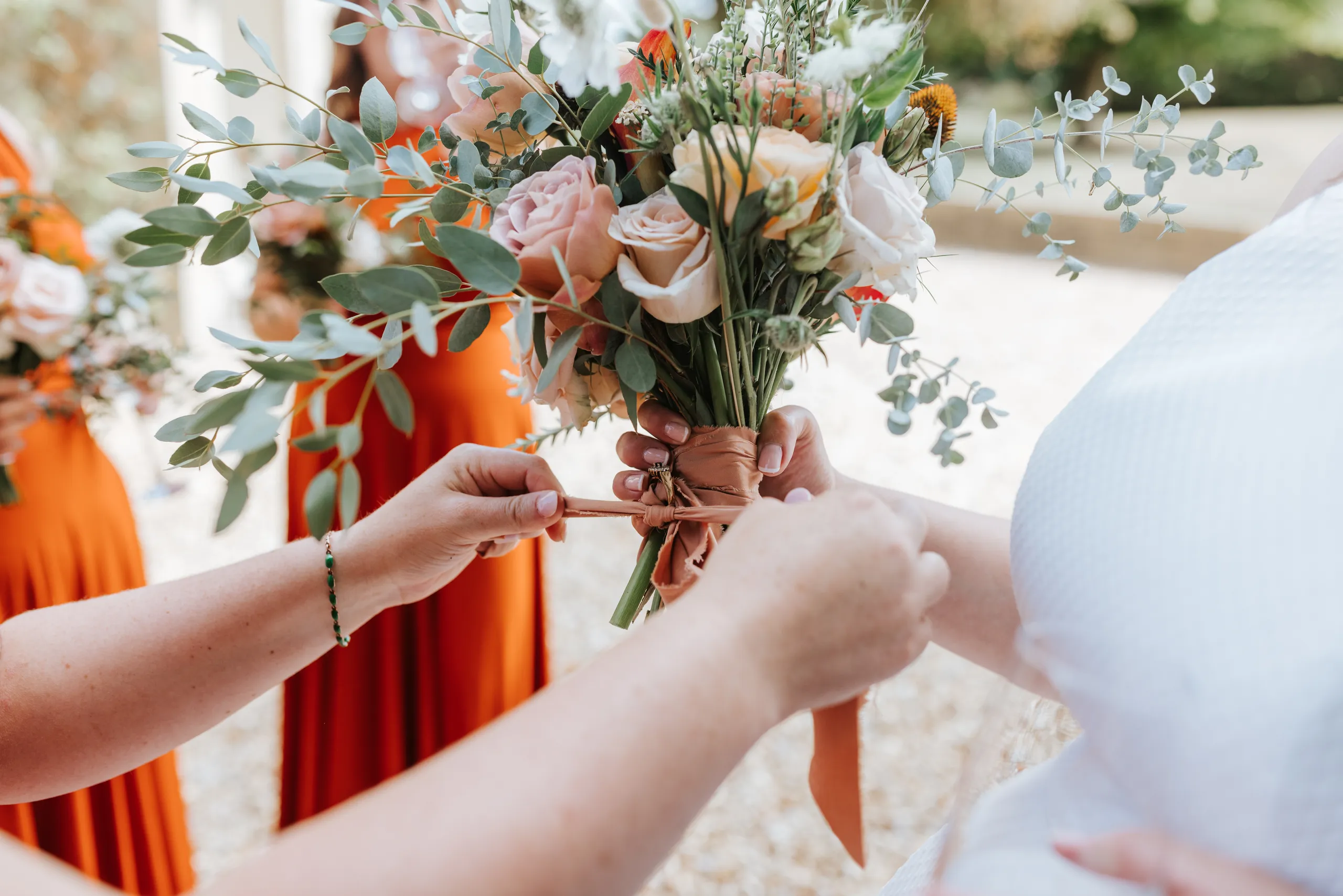 Hands tying a ribbon around a bridal bouquet of pale roses and eucalyptus greenery