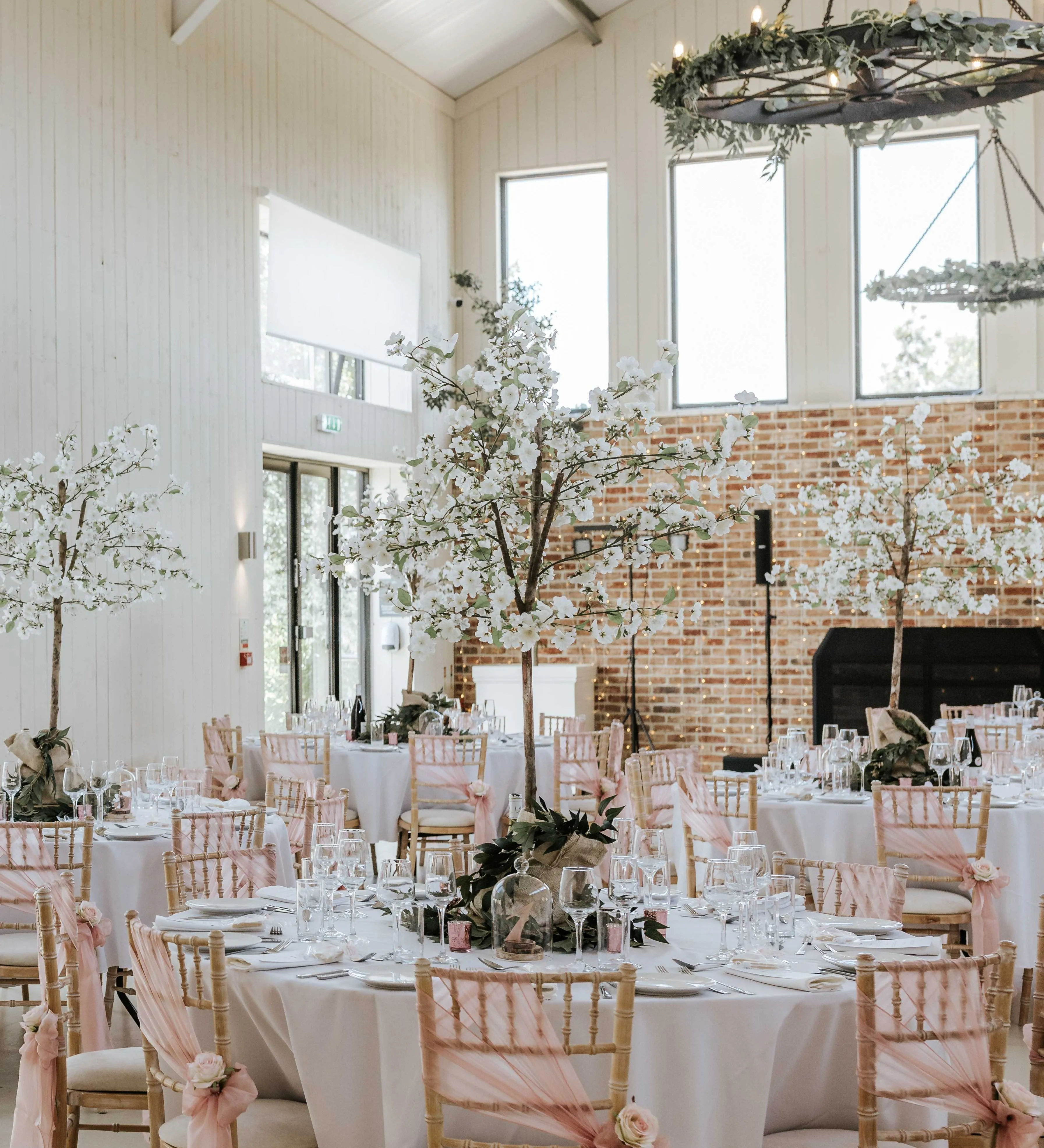 Elegant wedding reception tables in a bright barn venue with blossom centrepieces and pink chair sashes