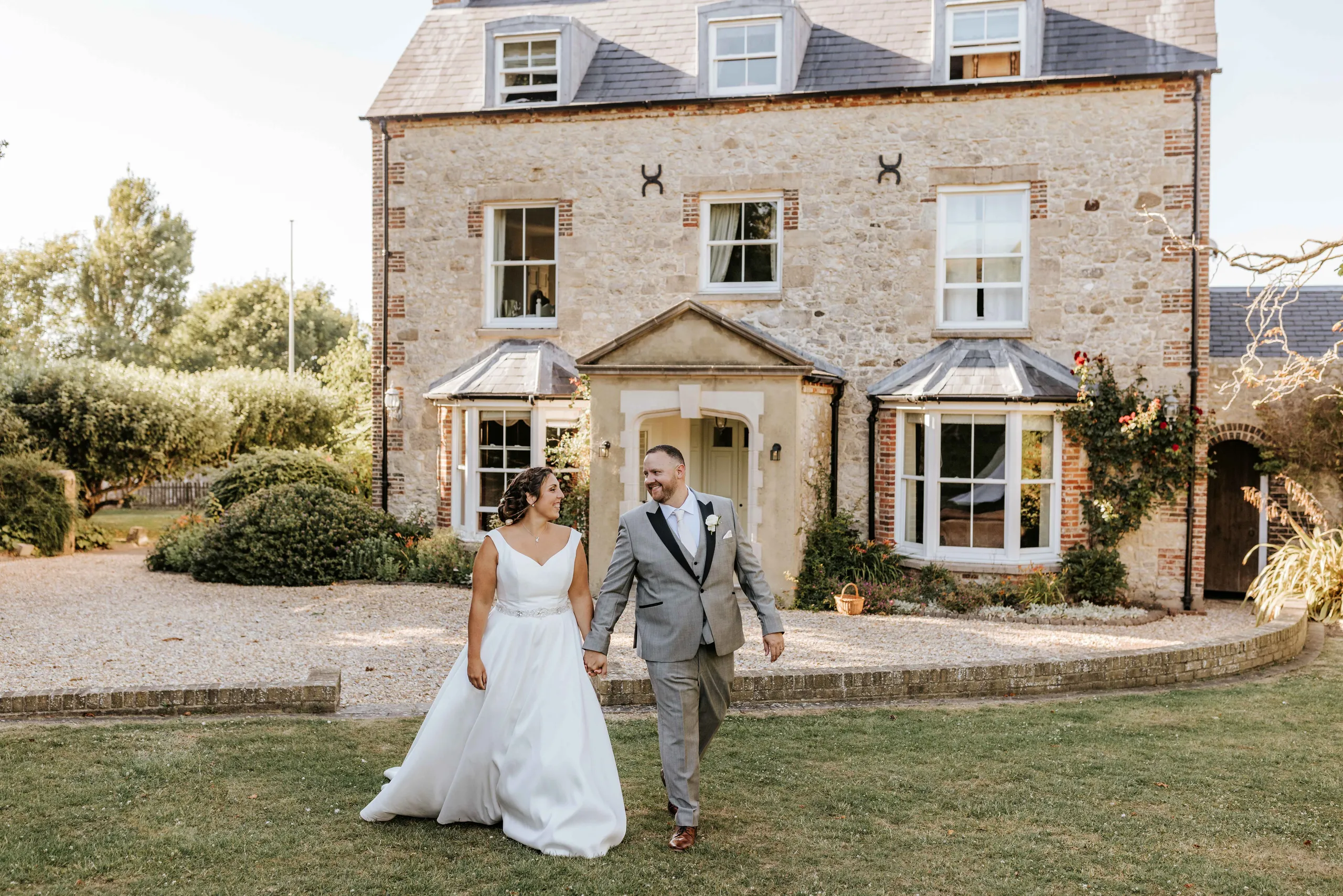 Bride and groom holding hands in front of a stone country house