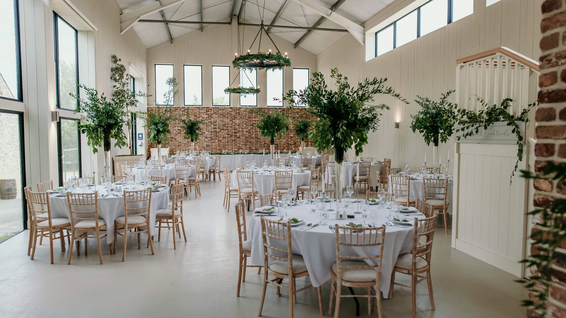 Bright barn wedding reception with round tables, white linens and greenery centrepieces