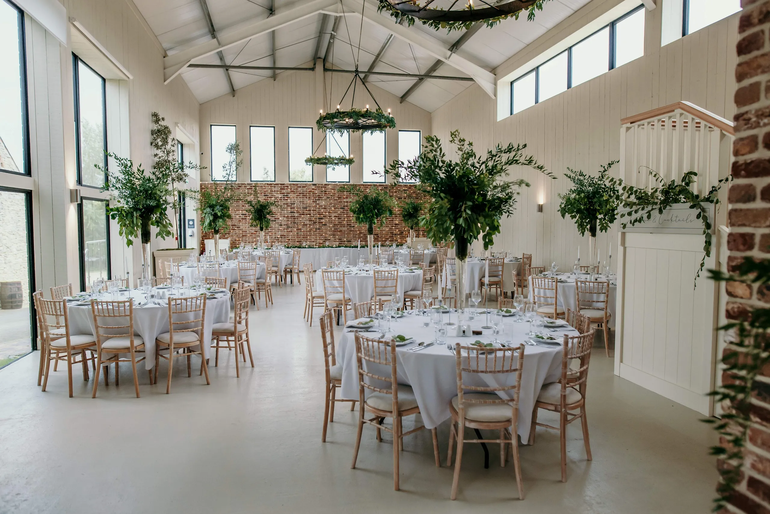 Bright barn wedding reception with round tables, white linens and greenery centrepieces