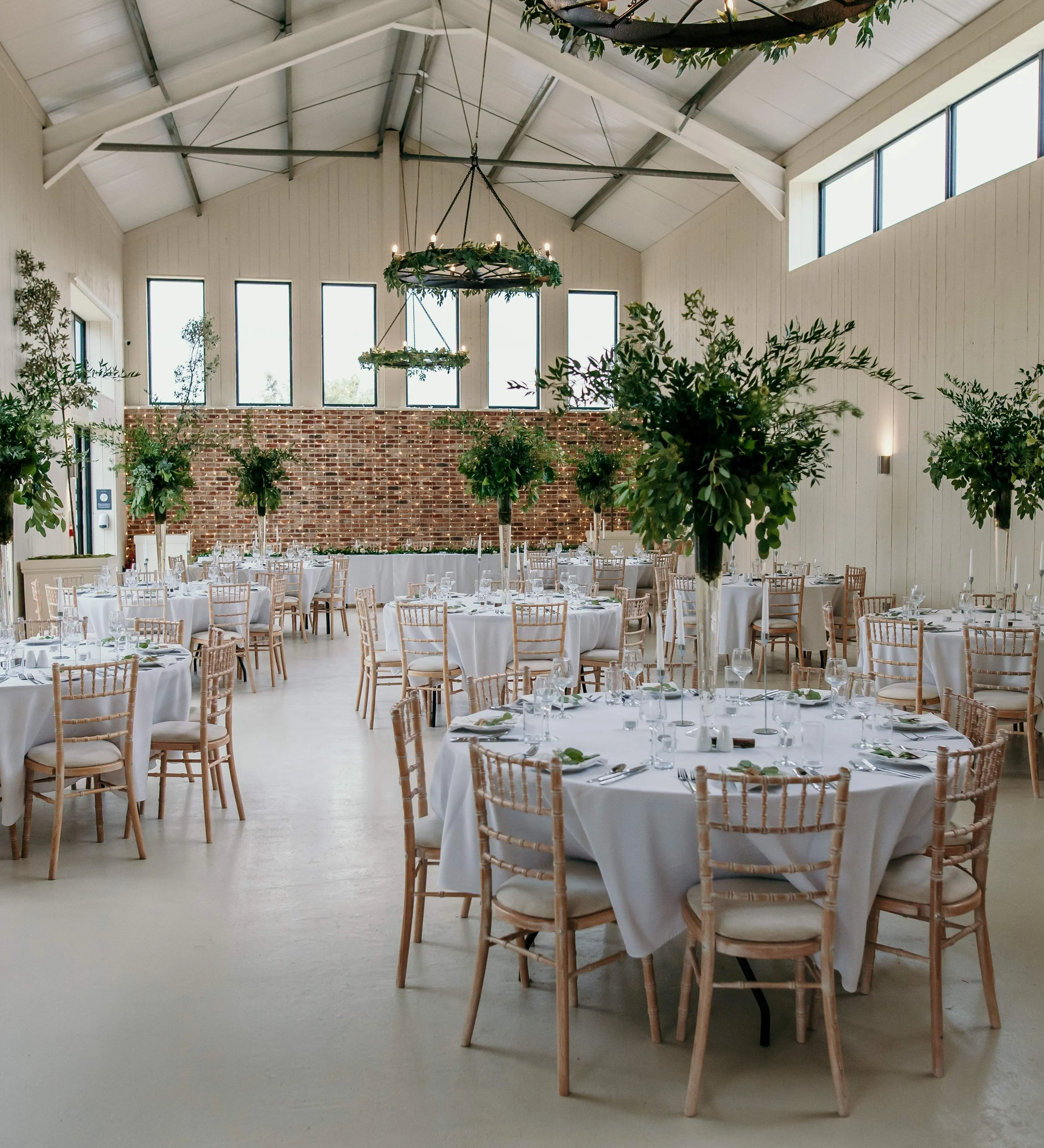 Bright barn wedding reception with round tables, white linens and greenery centrepieces