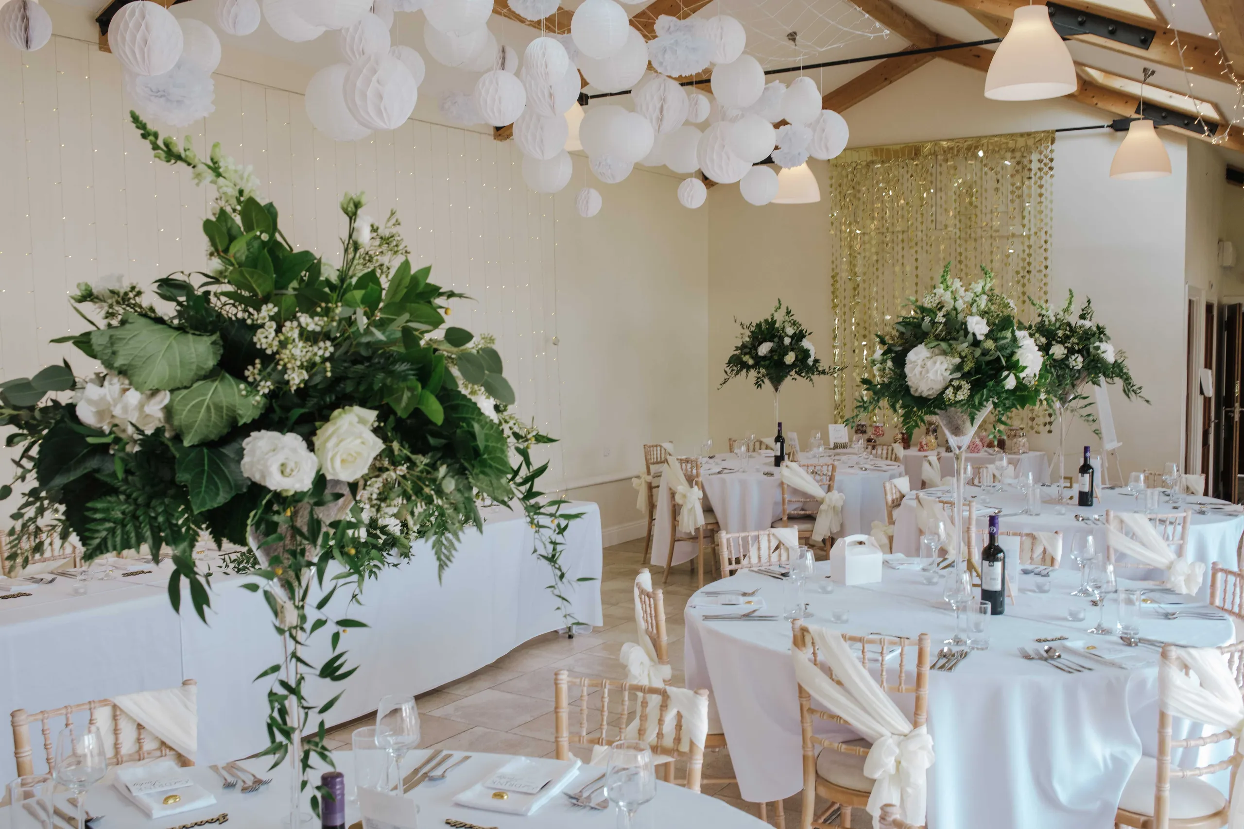 Wedding reception room with round tables, white paper lanterns and tall floral centrepieces