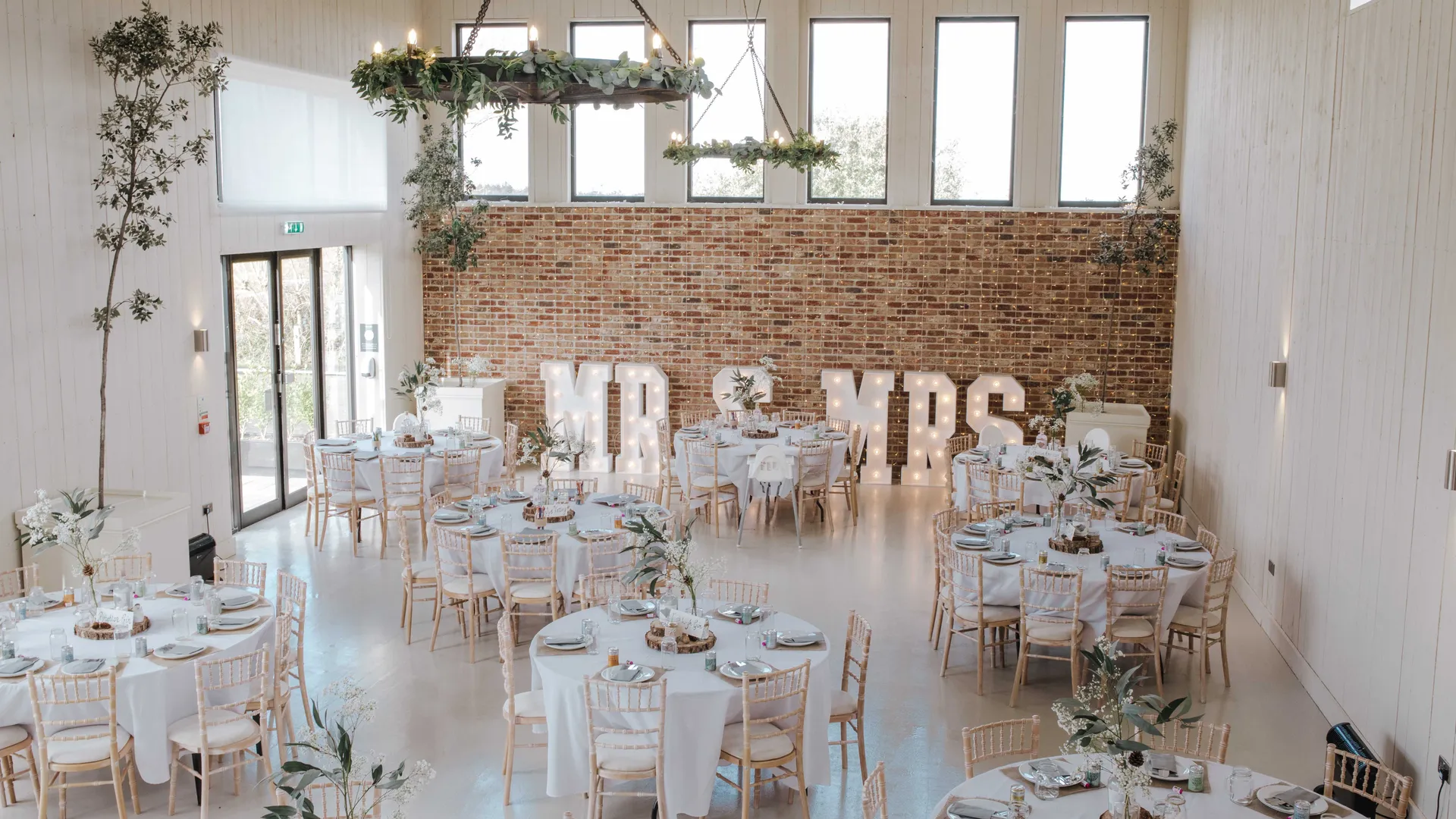 Rustic wedding reception room with round tables, floral centrepieces and illuminated 