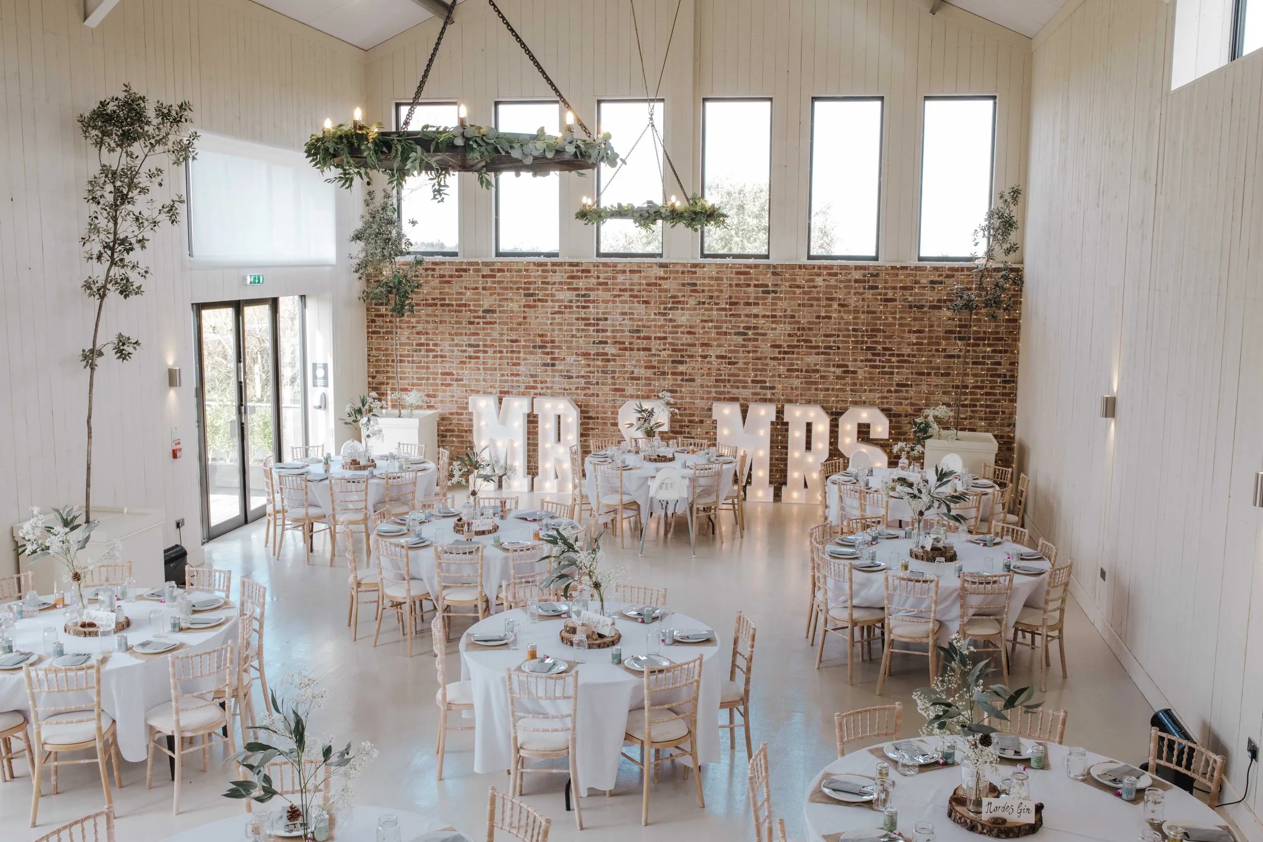Rustic wedding reception room with round tables, floral centrepieces and illuminated 