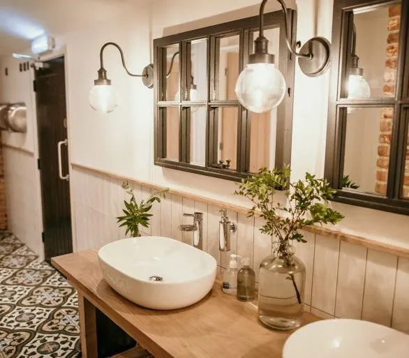 Rustic bathroom with double basins, patterned tile floor, and wall mirrors with globe lights
