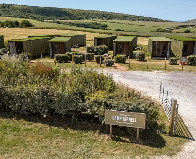 Green container cabins at Camp Tapnell set in rolling countryside with a welcome sign by the entrance