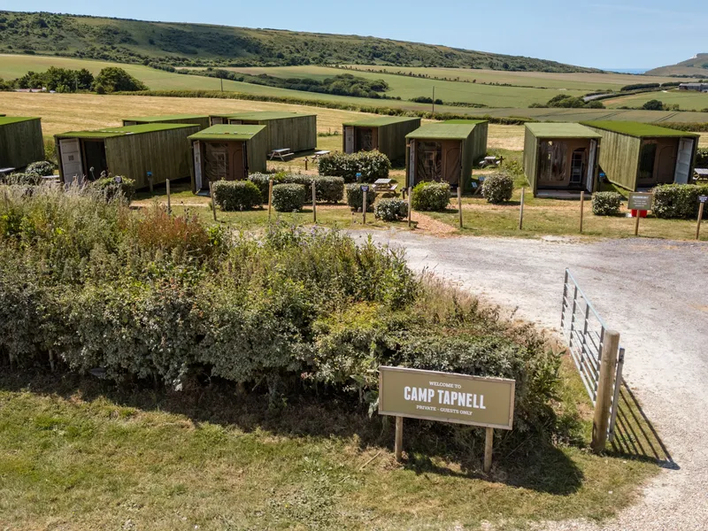 Green container cabins at Camp Tapnell set in rolling countryside with a welcome sign by the entrance