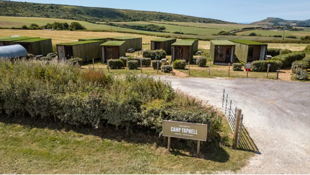 Green container cabins at Camp Tapnell set in rolling countryside with a welcome sign by the entrance