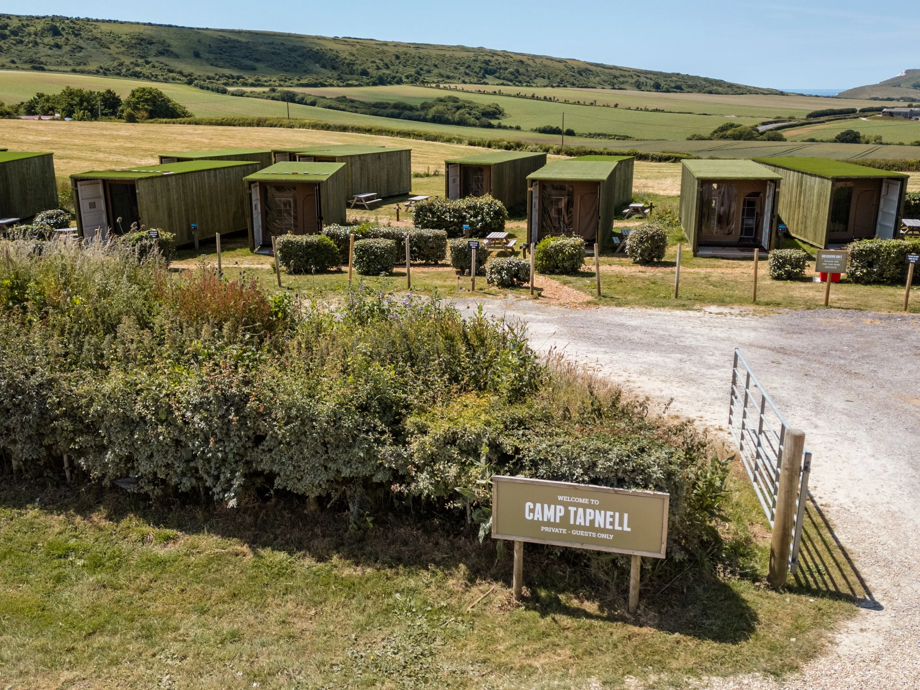 Green container cabins at Camp Tapnell set in rolling countryside with a welcome sign by the entrance