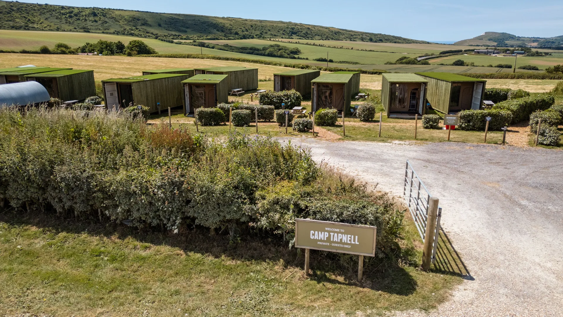 Green container cabins at Camp Tapnell set in rolling countryside with a welcome sign by the entrance