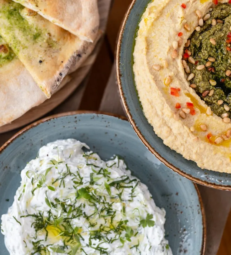 Pita bread wedges with a selection of dips, including hummus topped with pesto and pine nuts and a herby yoghurt dip