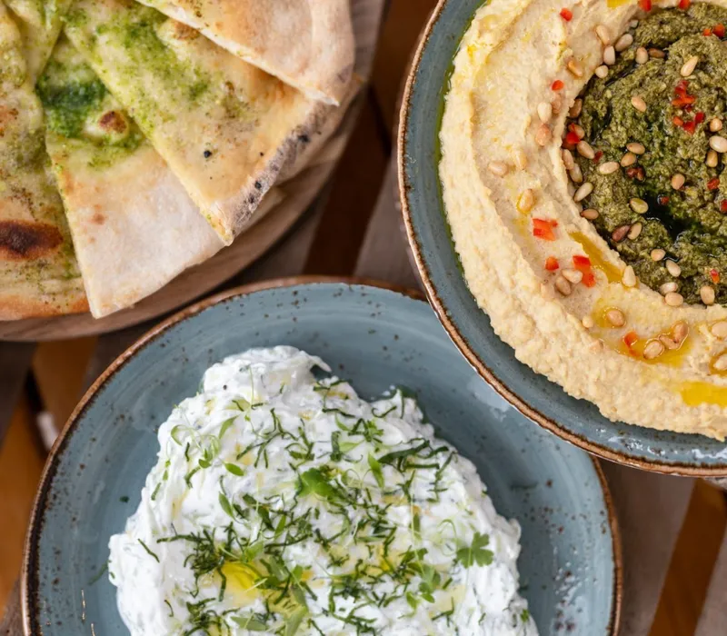 Pita bread wedges with a selection of dips, including hummus topped with pesto and pine nuts and a herby yoghurt dip