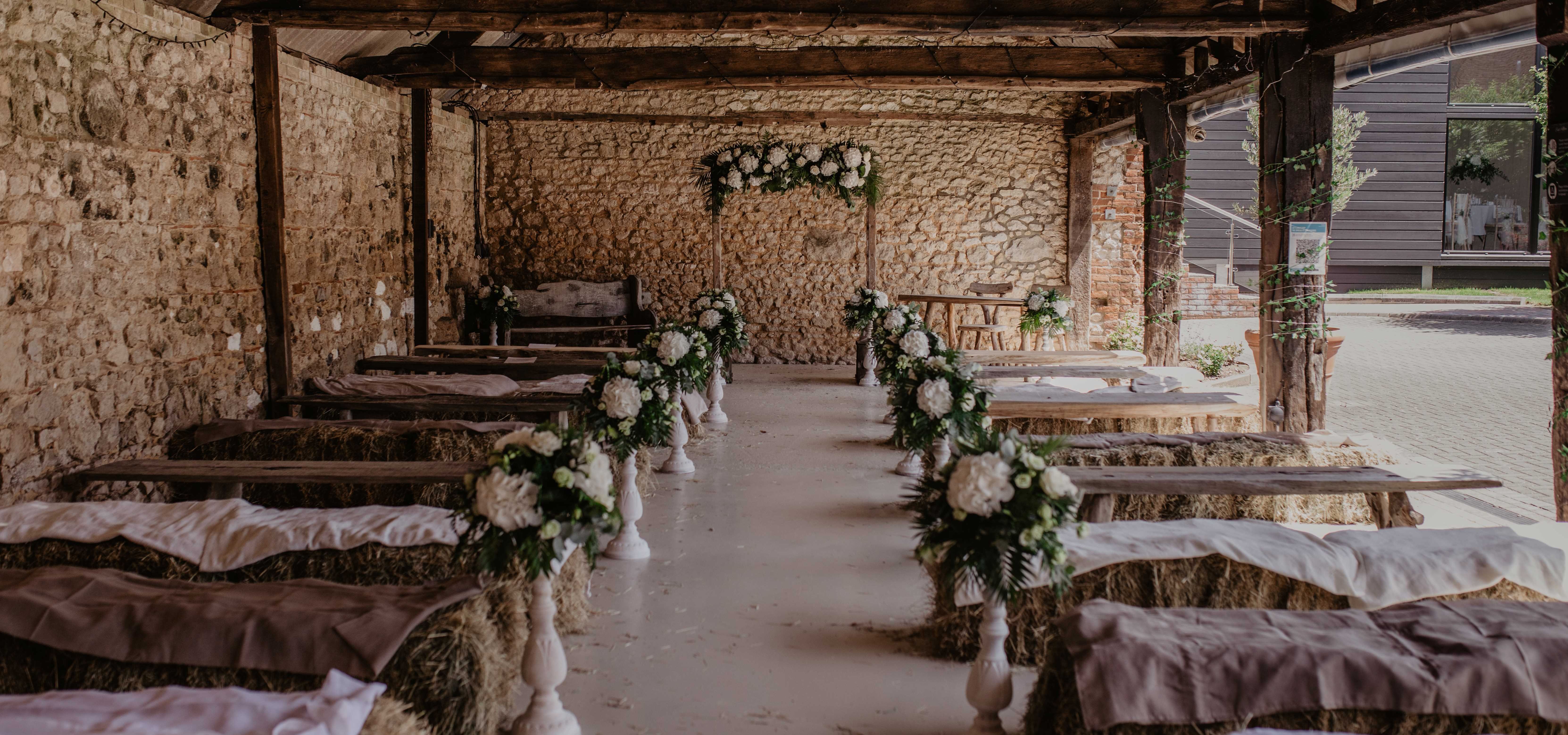 Rustic barn wedding ceremony set-up with hay bale seating and white floral arrangements