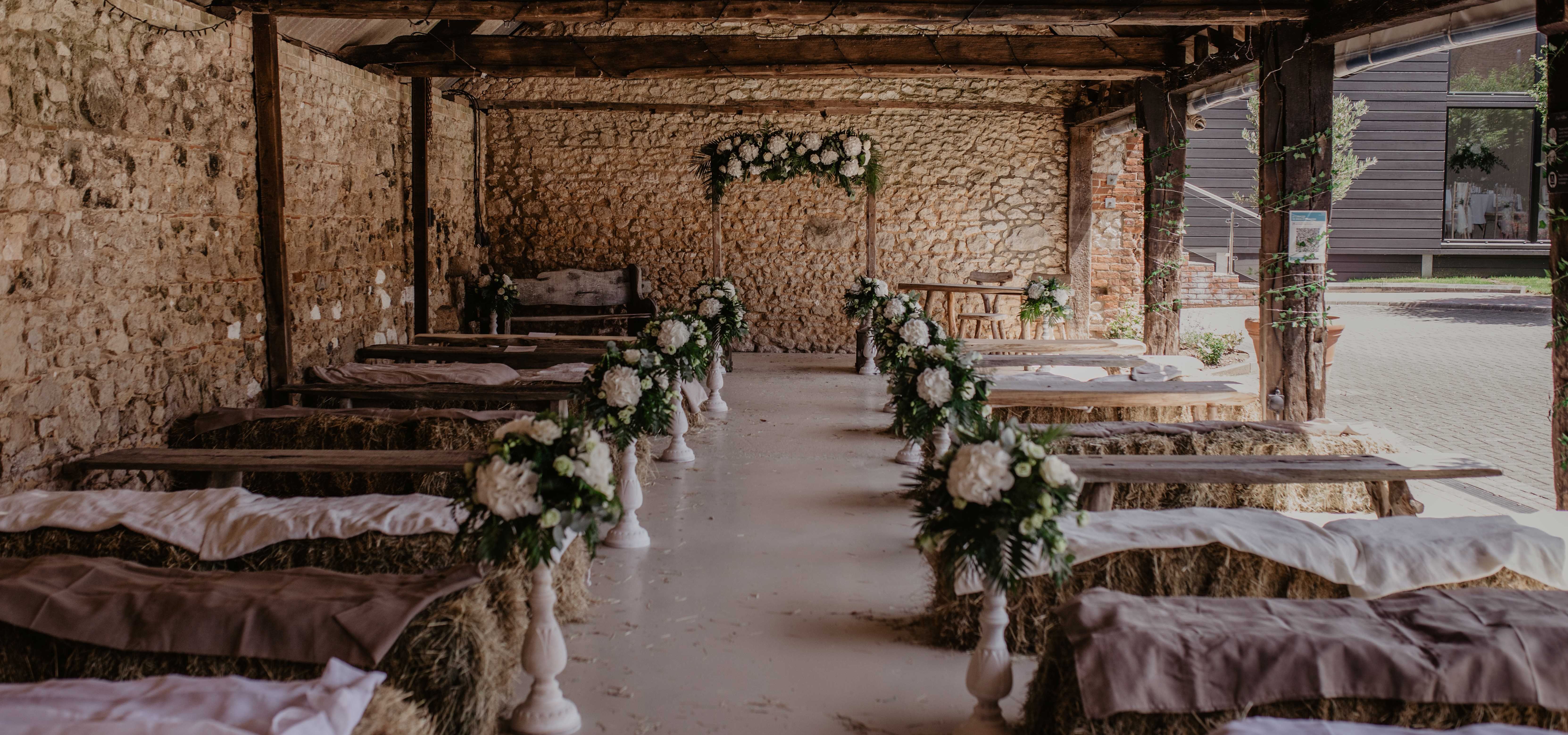 Rustic barn wedding ceremony set-up with hay bale seating and white floral arrangements