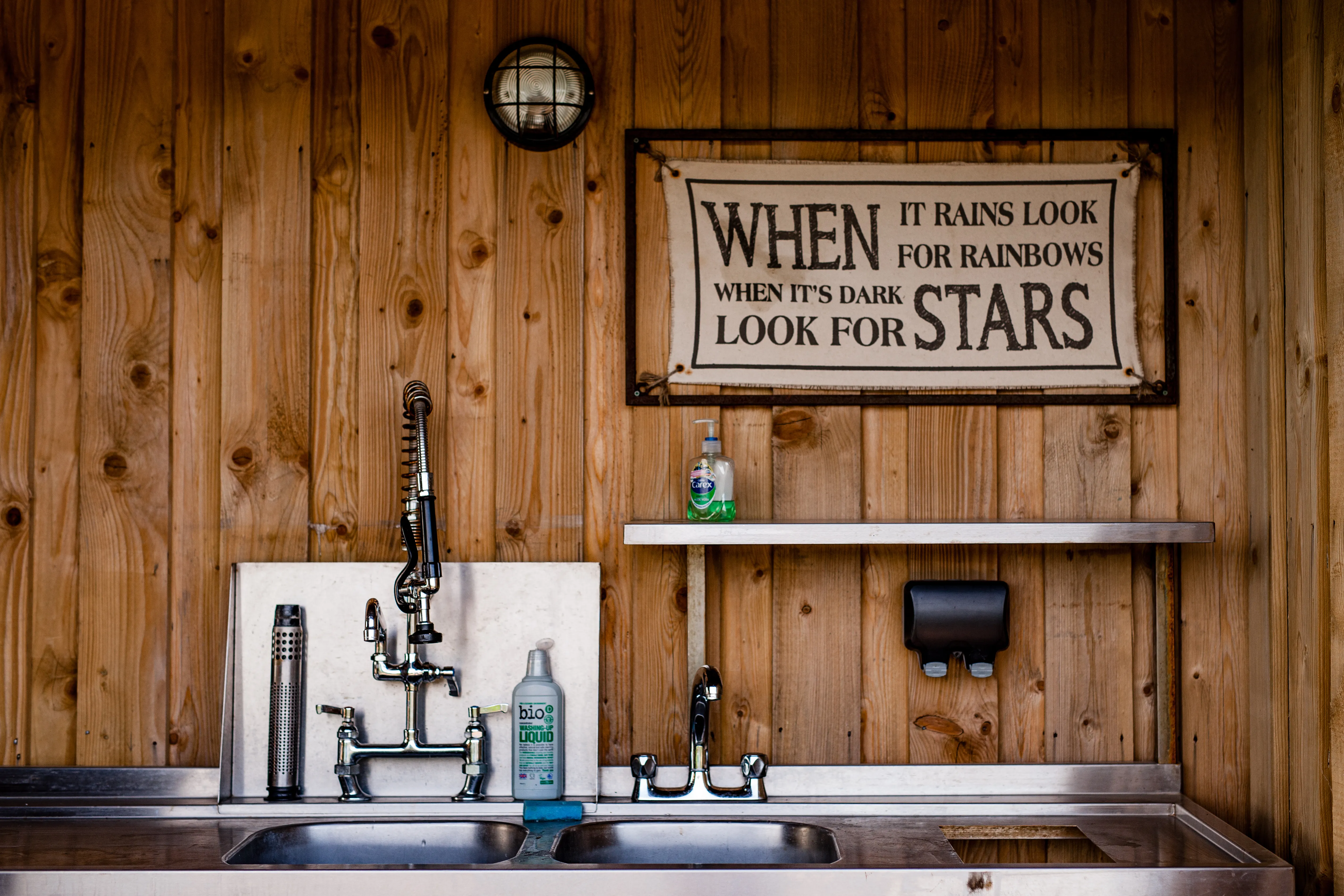 Stainless steel double sink and taps against a wooden wall with a sign reading 