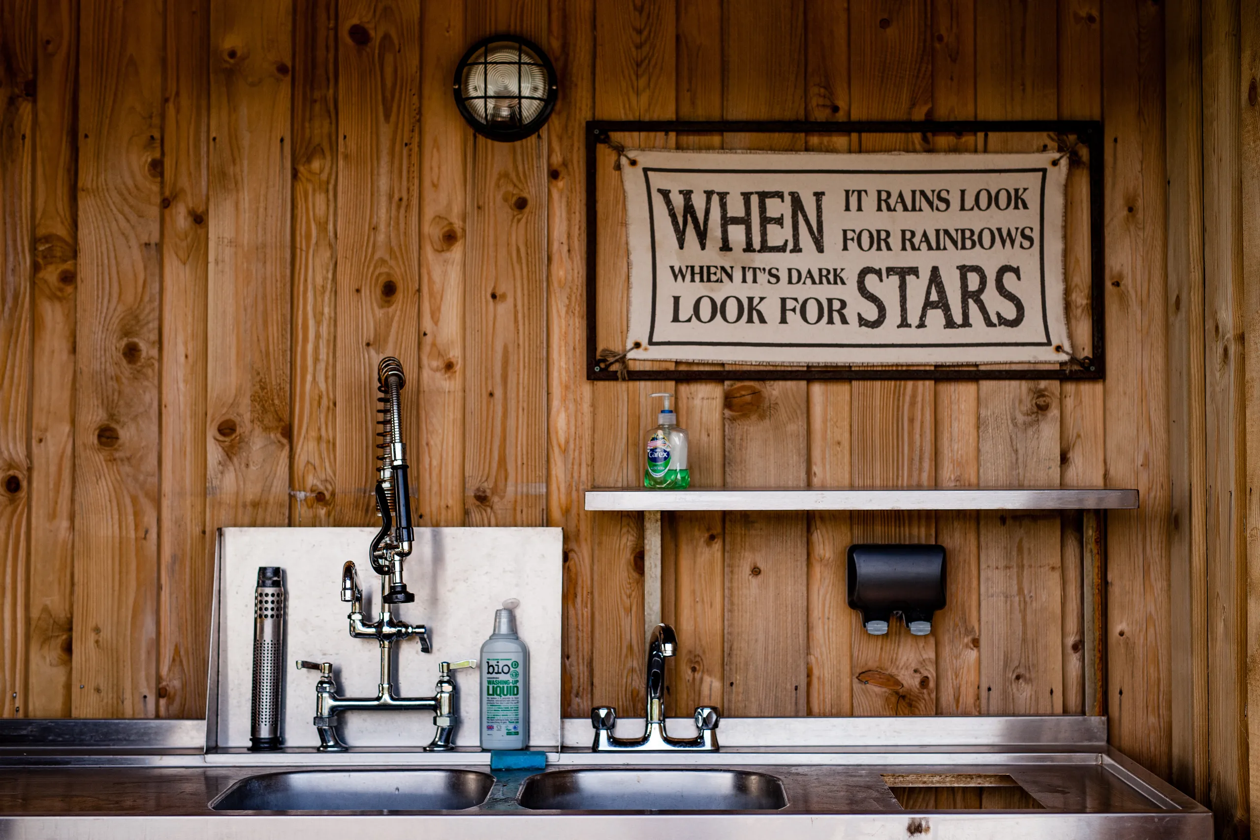Stainless steel double sink and taps against a wooden wall with a sign reading 