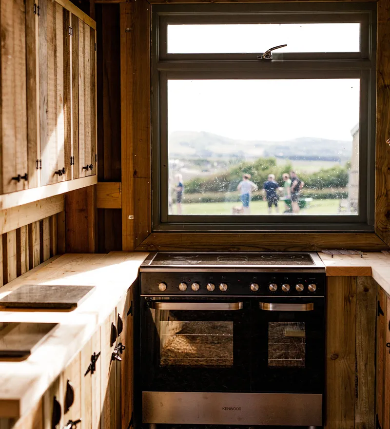 Rustic wooden cabin kitchen with double oven and window view over fields