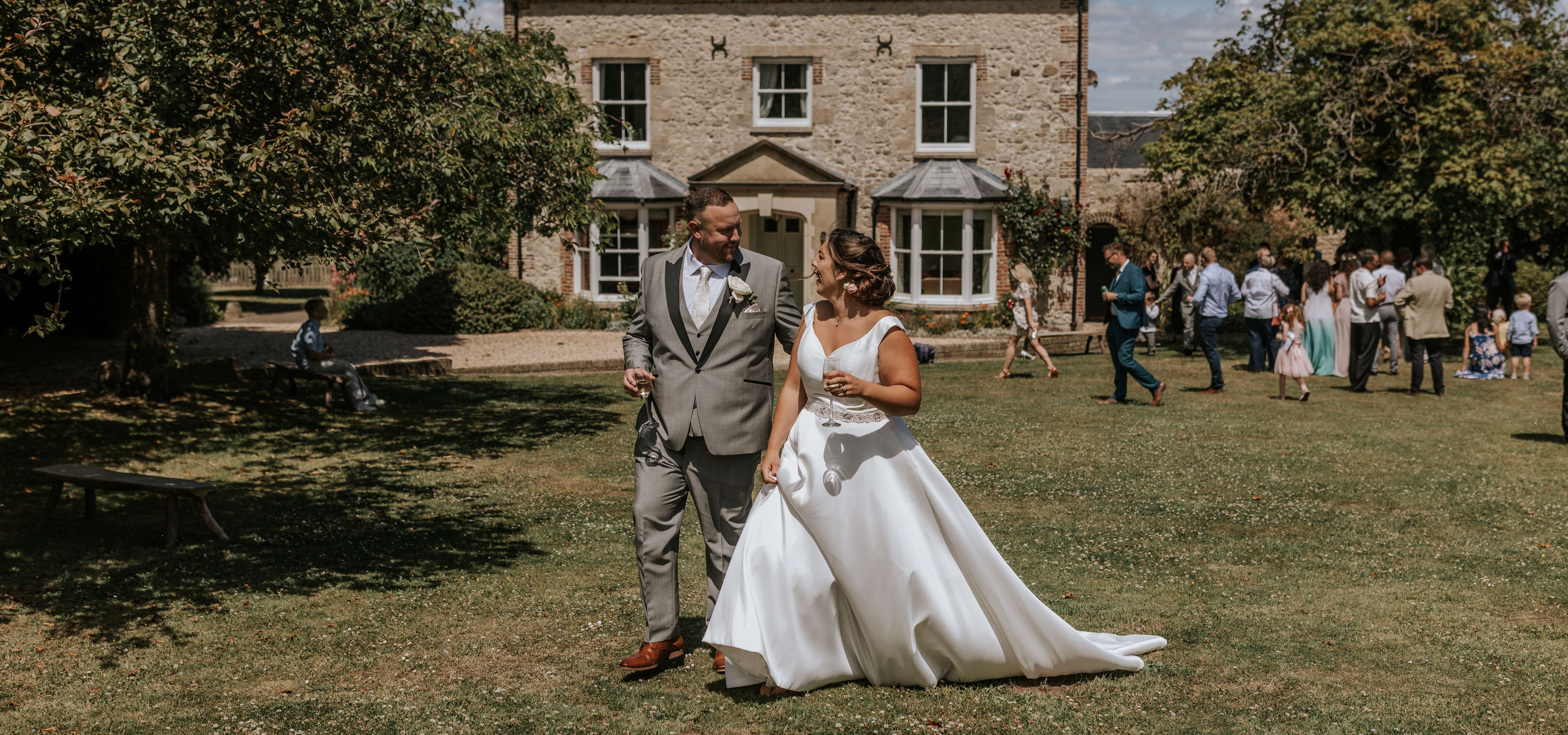 Bride and groom walking on a lawn in front of a stone country house during an outdoor wedding reception