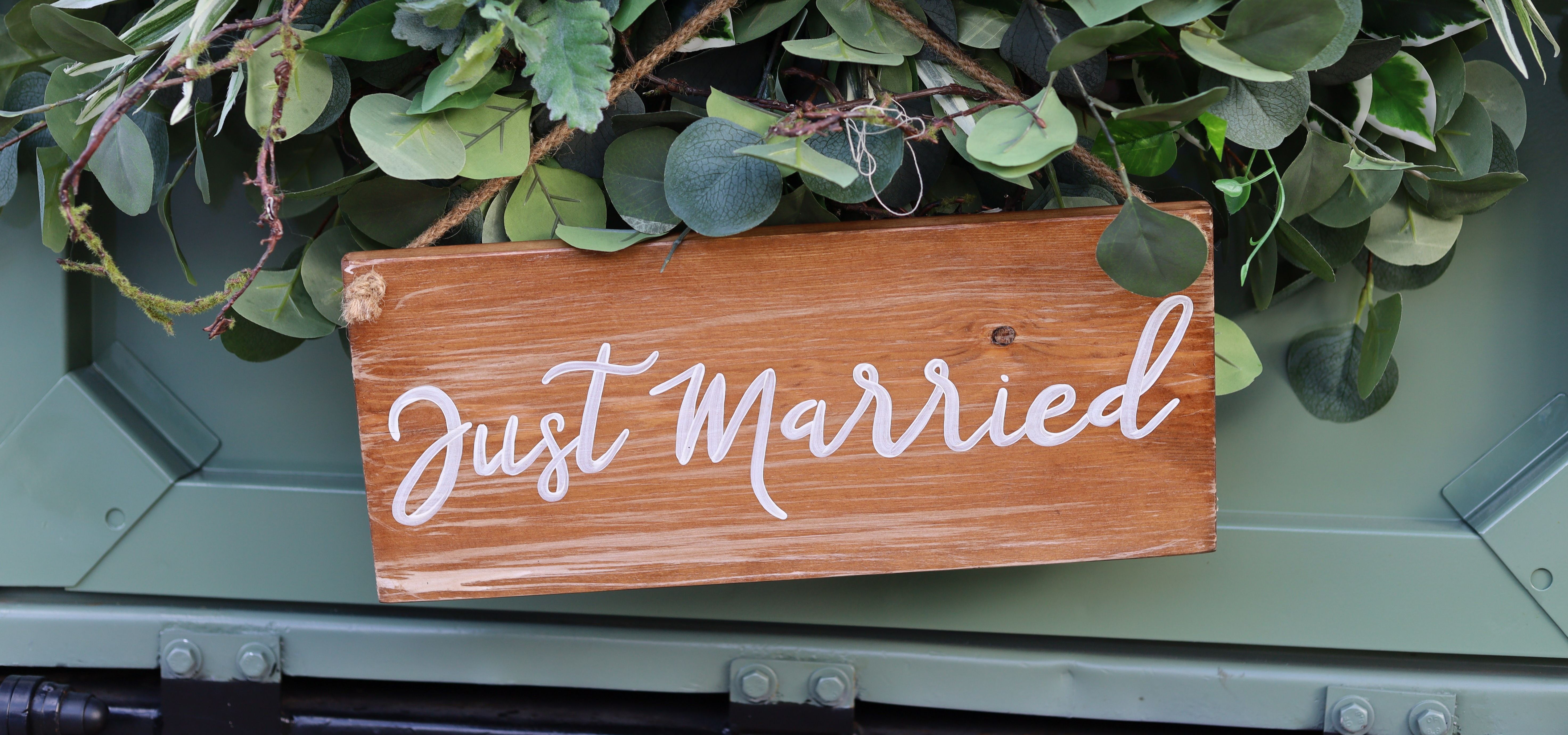Wooden "Just Married" sign hanging among green foliage
