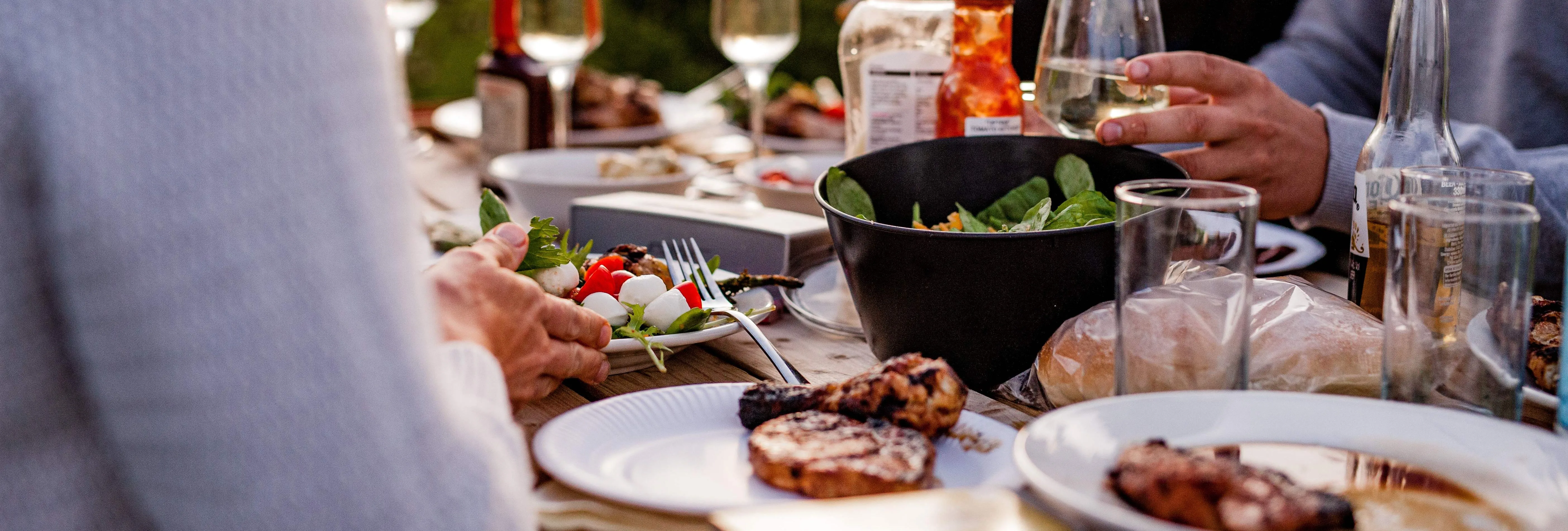 Friends sharing an outdoor meal at a table with wine glasses and plates of food at sunset